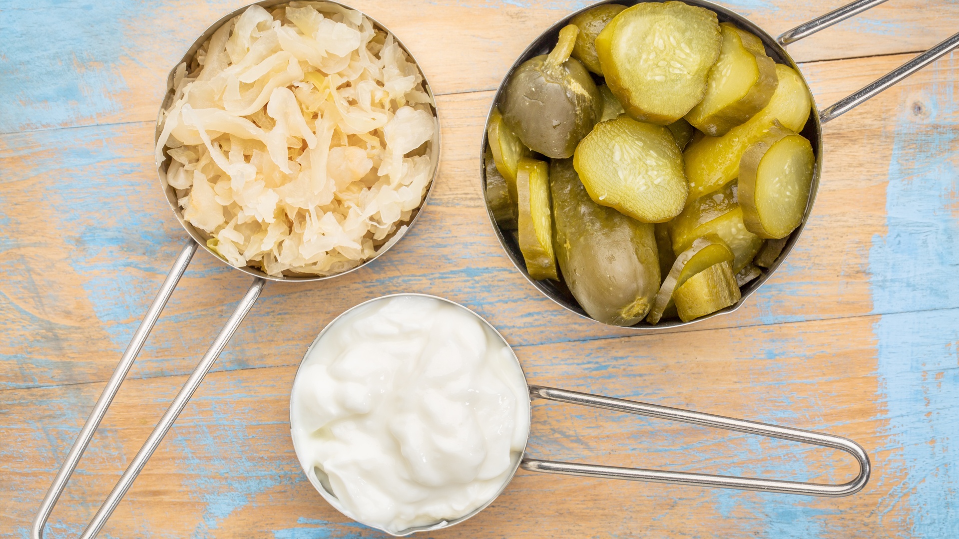 Three cups of fermented foods: sauerkraut, pickles and yogurt.