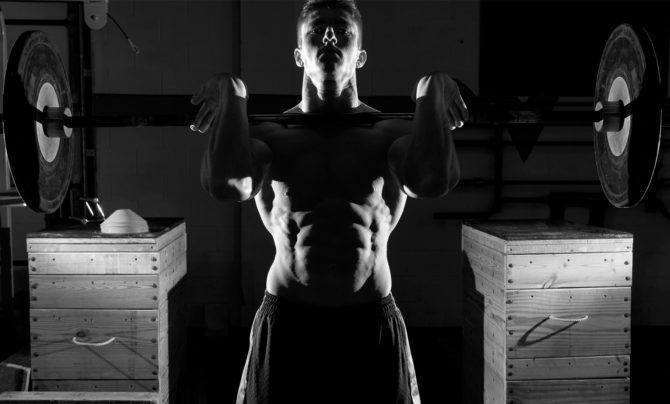 Weight lifting safely: a muscular young man securely holds a barbell in the front rack position.