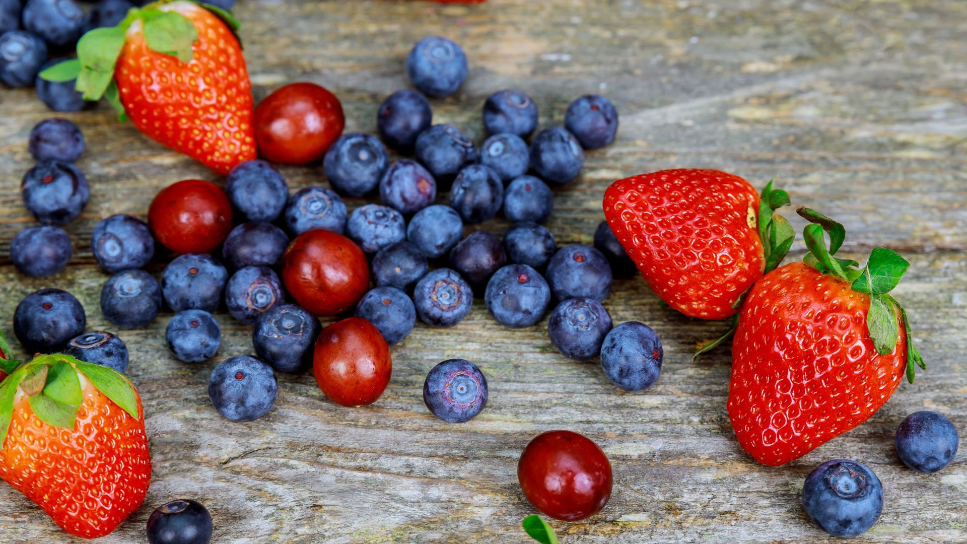 A pile of blueberries and strawberries sit atop a wooden table. 