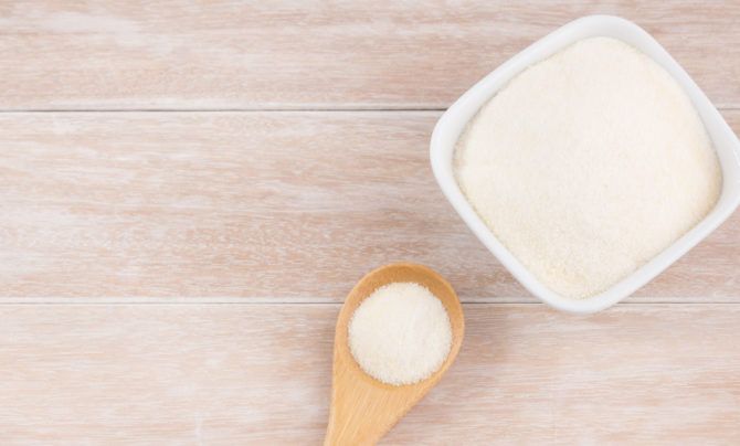 A wooden spoon and ceramic bowl filled with collagen powder.