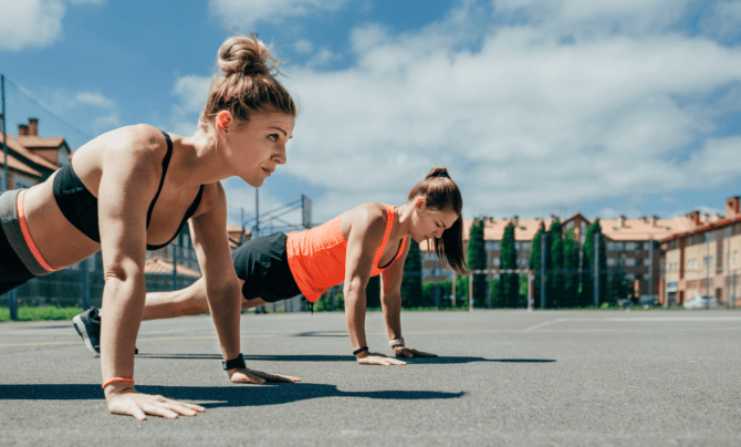 two women doing pushups outside