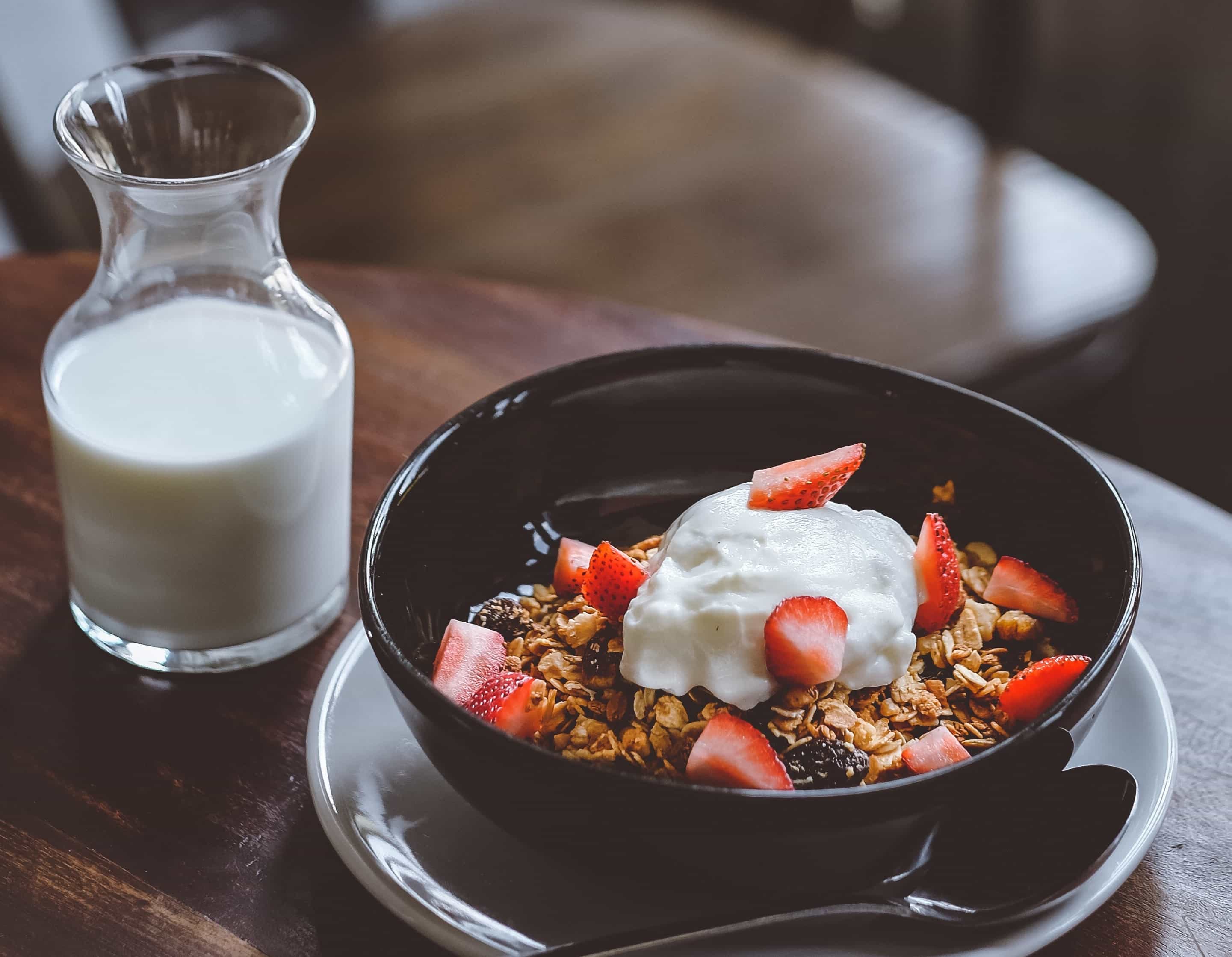 a glass of milk next to a bowl of yogurt and granola