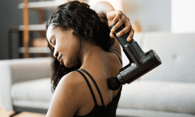 woman using a massage gun on her back